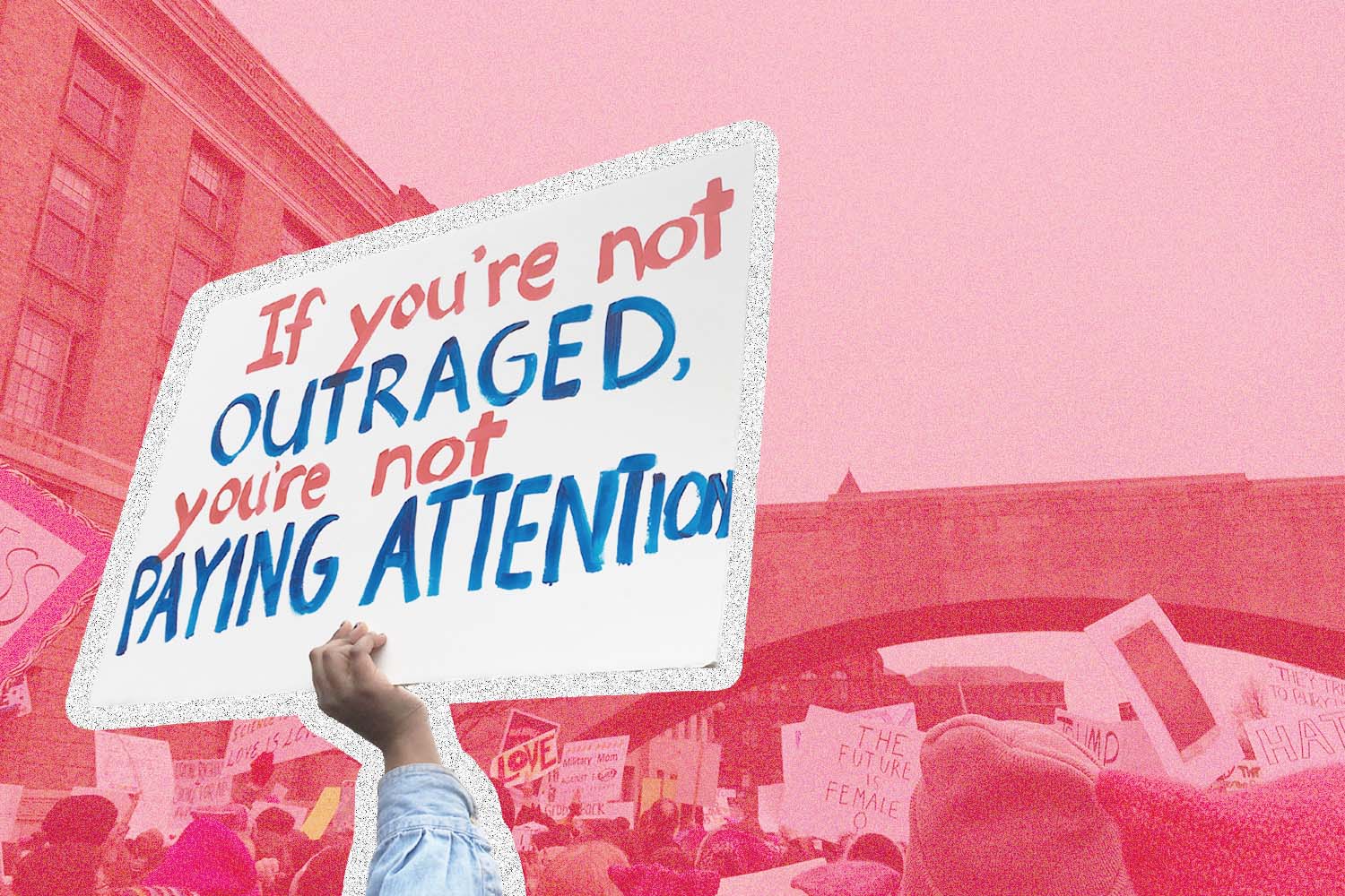 Person holding a sign that reads, "If you're not outraged, you're not paying attention"