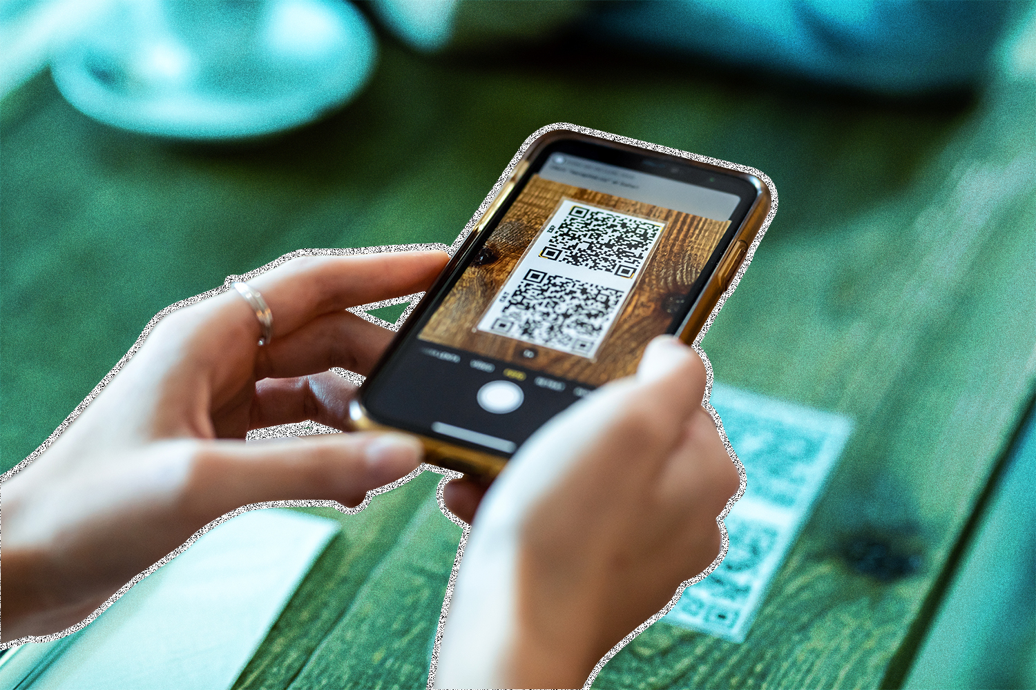 Two hands holding a smartphone over a table with a QR code on the smartphone screen