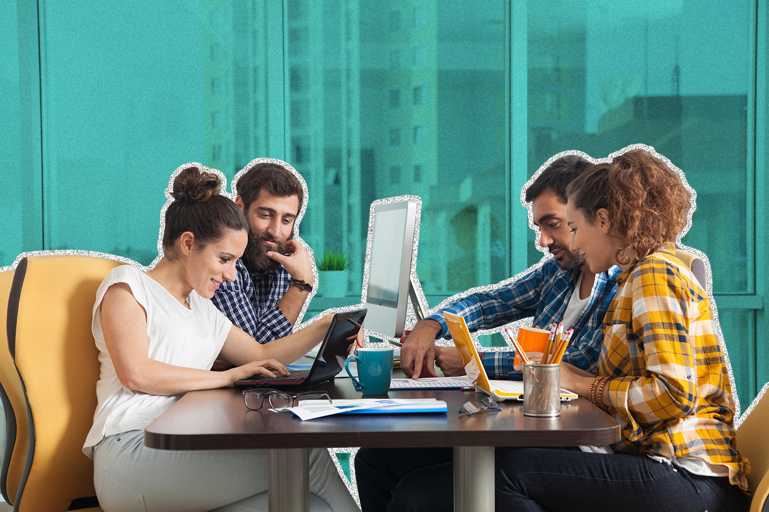 Four employees sitting at a table looking at laptops and interacting with one another.